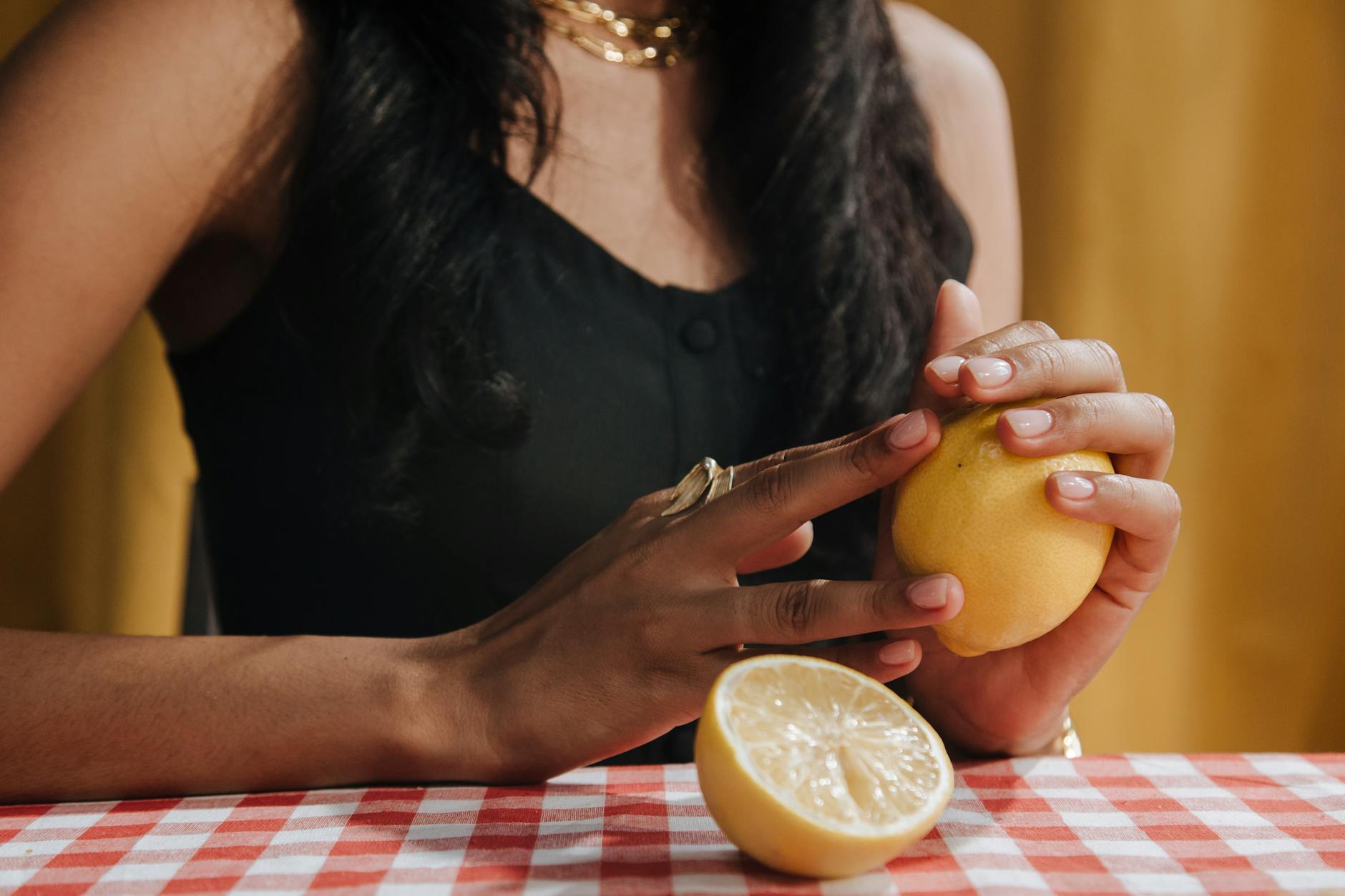 A hand with white nails holding a fresh lemon on a soft pink background