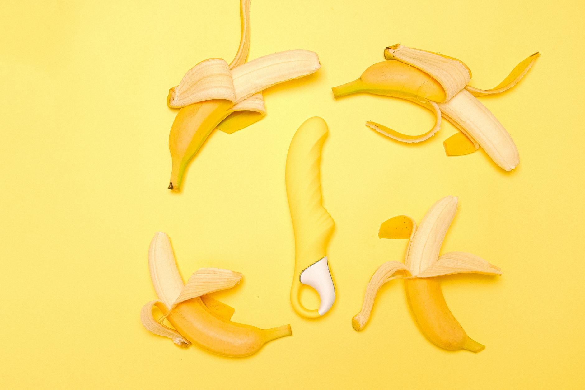 Yellow lemon-shaped silicone vibrator surrounded by peeled lemons on a bright yellow background