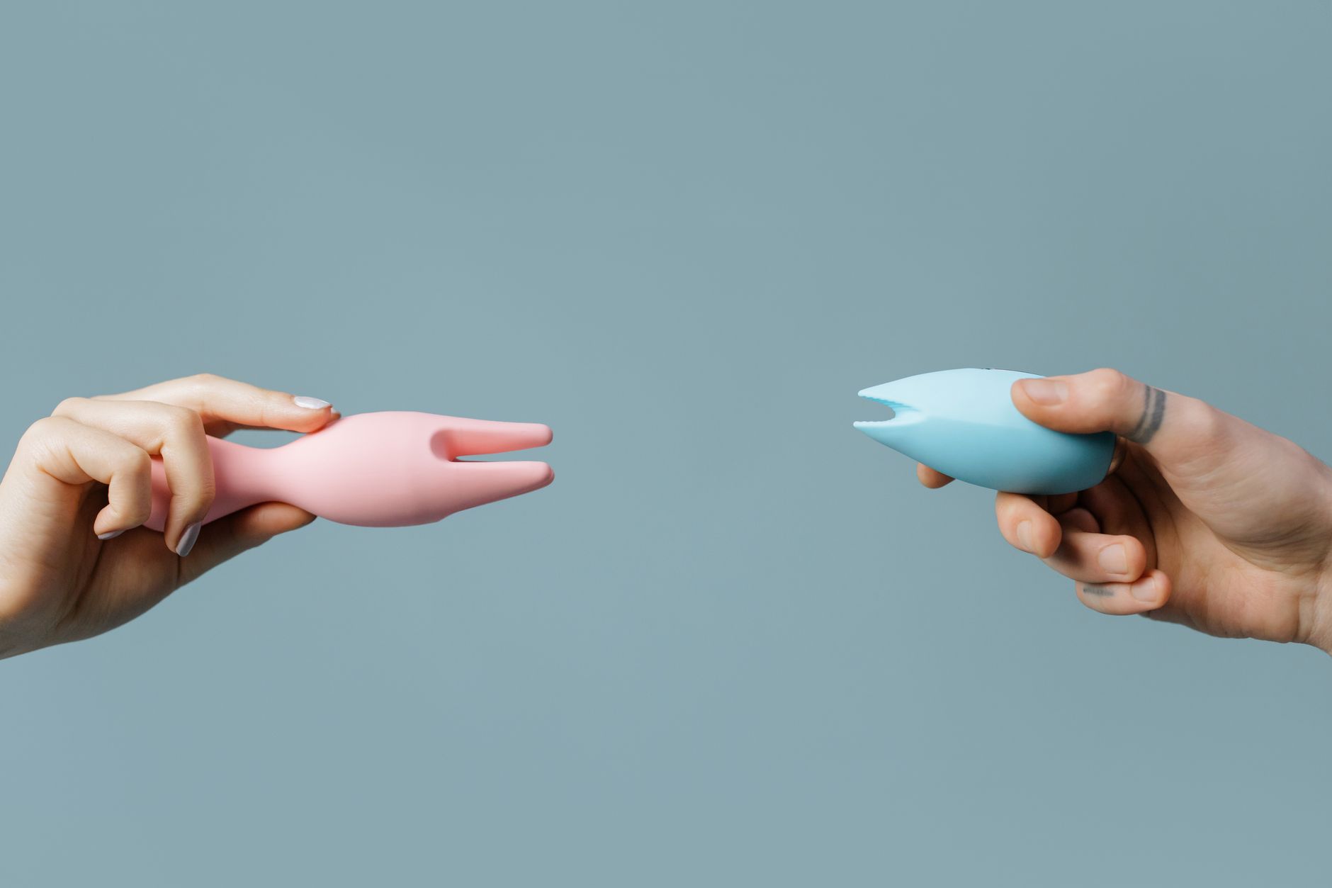 Hands holding pastel-colored silicone vibrators against a soft background