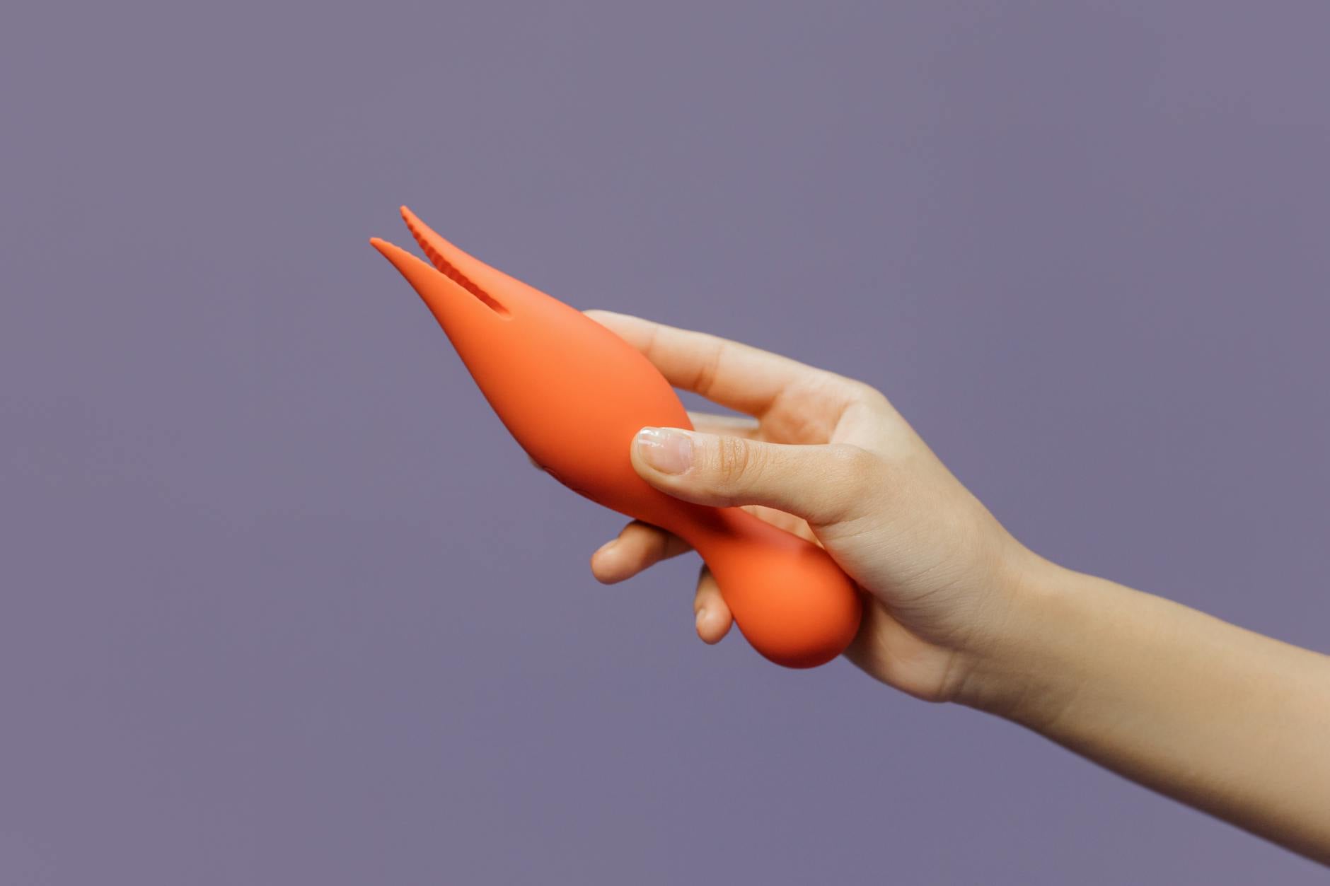 A hand holding a lemon vibrator against a minimalistic purple backdrop, showcasing modern sensuality