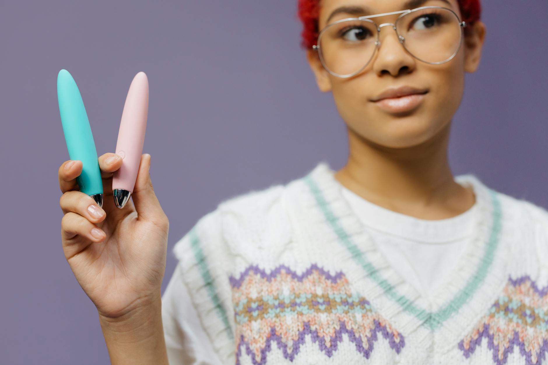 Woman holding colorful clitoral vibrators and tools for pleasure against a purple background