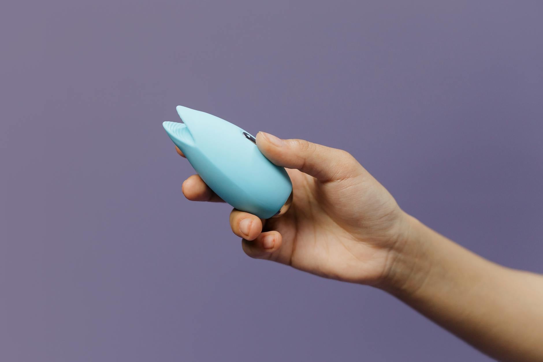 Woman with eyeglasses holding blue and pink clitoral vibrators in a thoughtful manner
