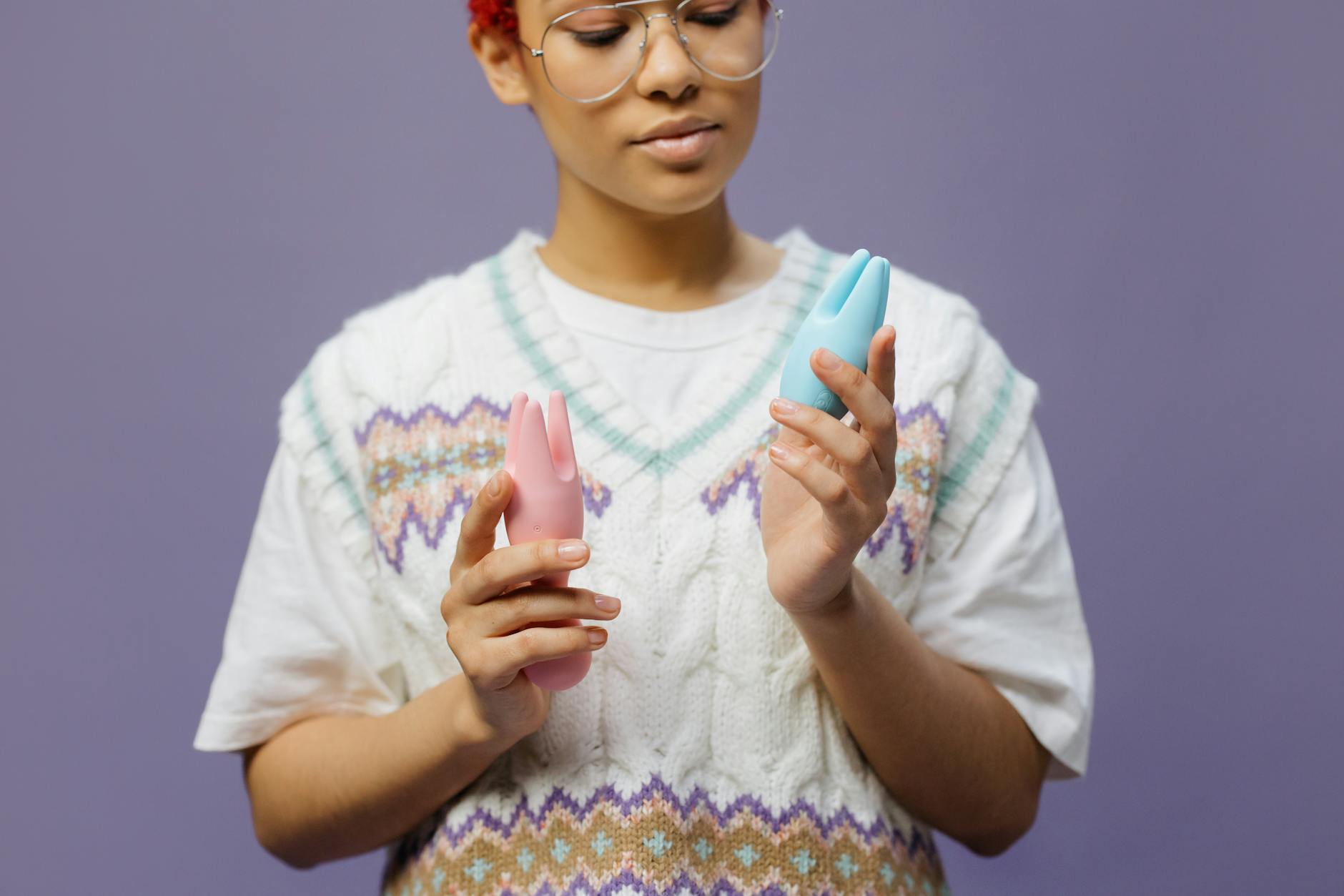Woman holding blue and pink silicone vibrators in a contemplative moment during personal exploration