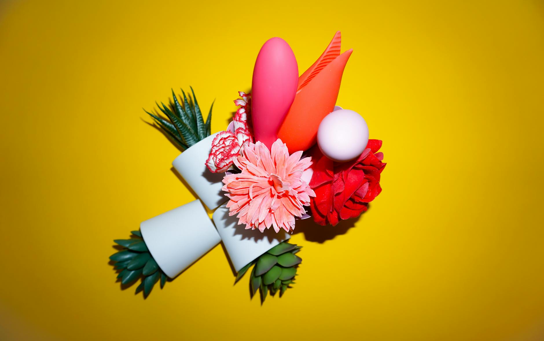 A hand reaching over a collection of colorful vibrators and adult toys on a table