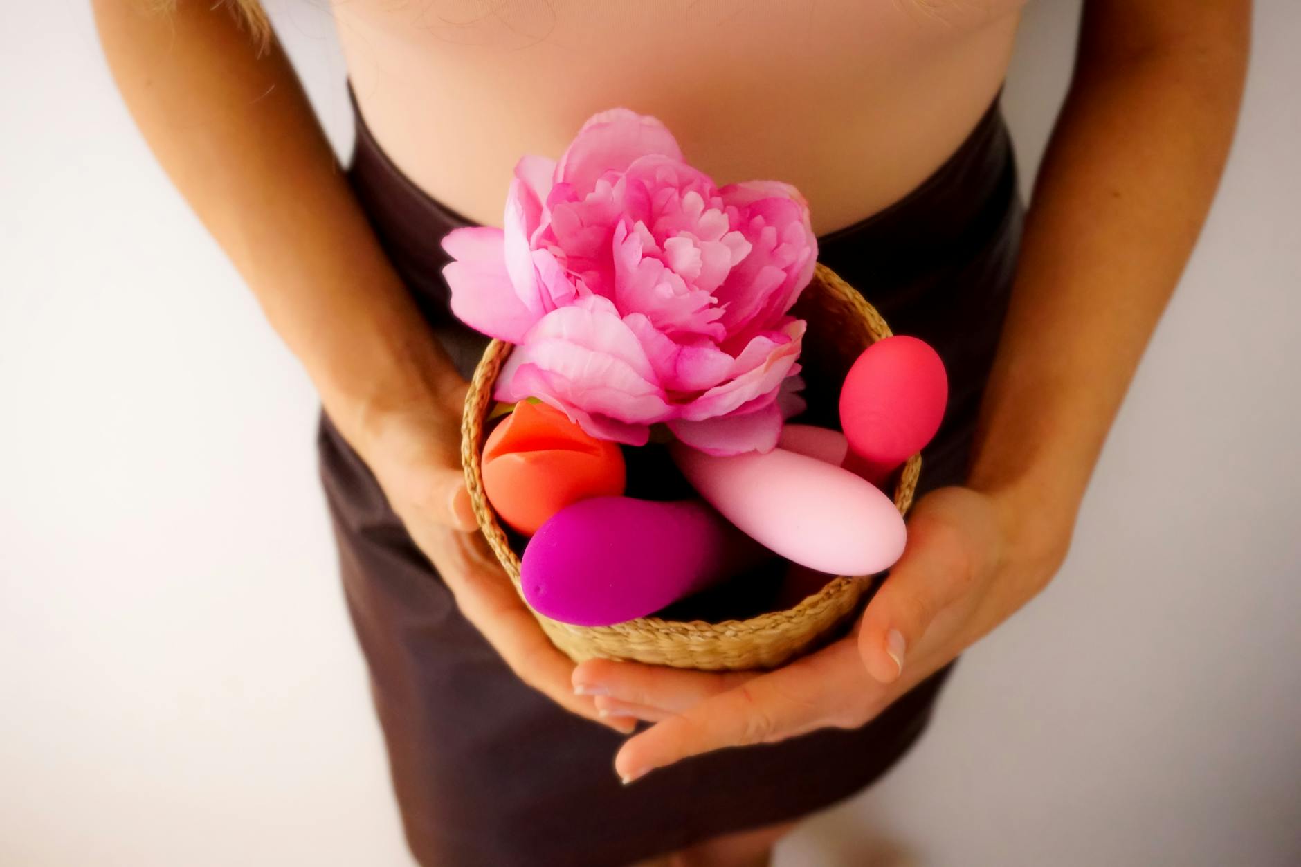 A basket of colorful vibrators and adult toys on a soft surface